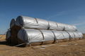 Heavy-duty tarp stretched tightly over 10 round hay bales with silver bungee cords on a sunny day